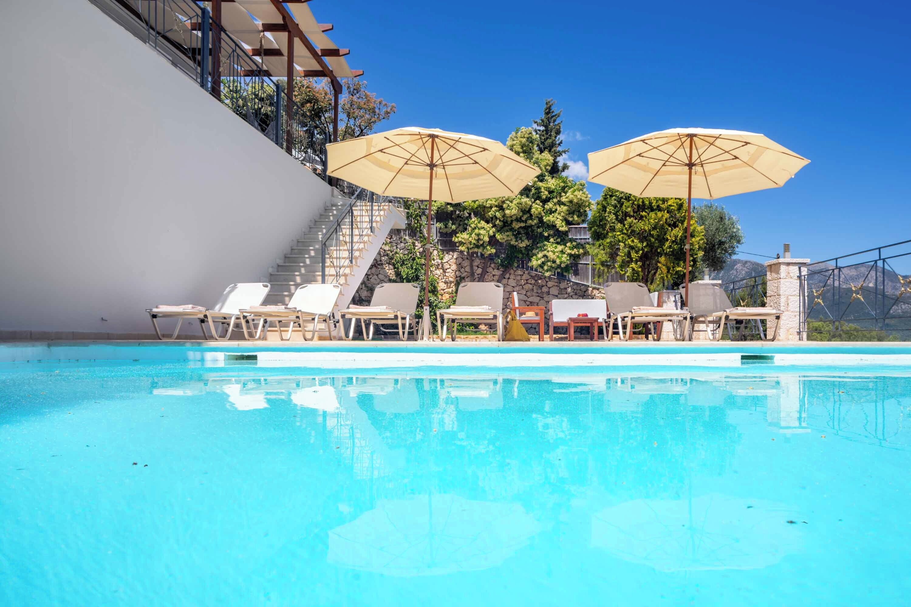 A swimming pool with lounge chairs and umbrellas, a staircase, and a stone wall with greenery.