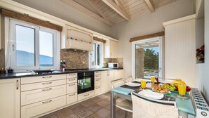 Eine moderne Küche mit Essbereich, ausgestattet mit einem Glastisch, weißen Schränken und Blick durch das Fenster.