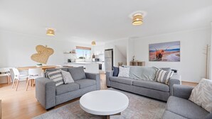 En moderne stue med to grå sofaer, et hvidt sofabord og et køkken i baggrunden.