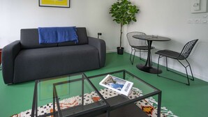Een zithoek met een bank, een klein tafeltje met stoelen, een potplant en een lijst met een afbeelding aan de muur.