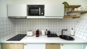 Een moderne keuken met een magnetron, broodrooster, waterkoker, spoelbak en een plant op een plank.