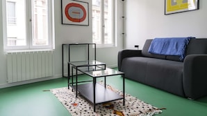 Een woonkamer met een grijze bank, een glazen salontafel en twee kunstwerken in lijsten aan de muur.