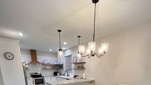 A modern kitchen with white cabinetry, a wooden dining table, and pendant lighting. - Love to fish! We have a dock  (Oak Island)
