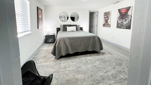 Un dormitorio con cama, mesita de noche, espejo y cuadros en las paredes.