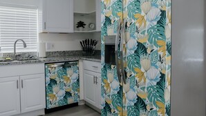 Una cocina con armarios blancos, un refrigerador de acero inoxidable y salpicadero con estampado floral.
