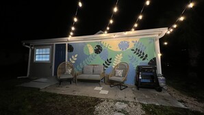 Una casa con un mural, dos sillas de mimbre y una parrilla.
