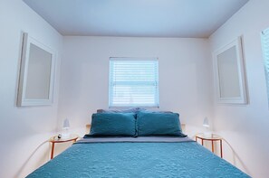 Una camera da letto con un letto, due comodini, una finestra con persiane e uno specchio fissato al muro.