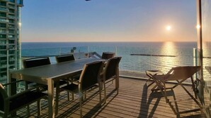 Une terrasse avec une table et des chaises, donnant sur une étendue d’eau et offrant une vue sur le coucher du soleil.