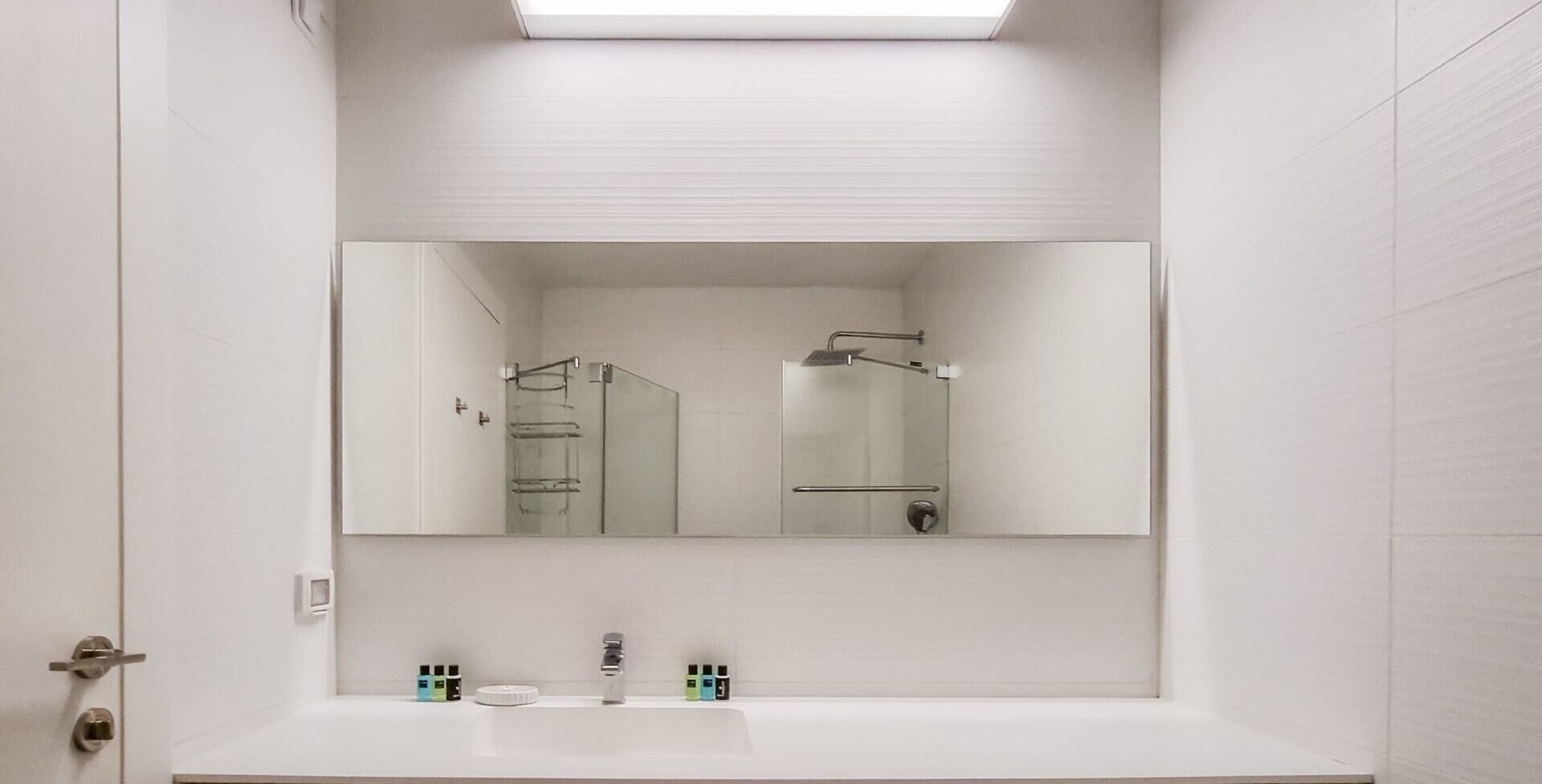 A modern bathroom with a large mirror, a shower, and a sink with toiletries.