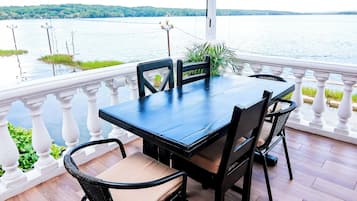 A covered outdoor seating area with a table and chairs, overlooking a body of water.