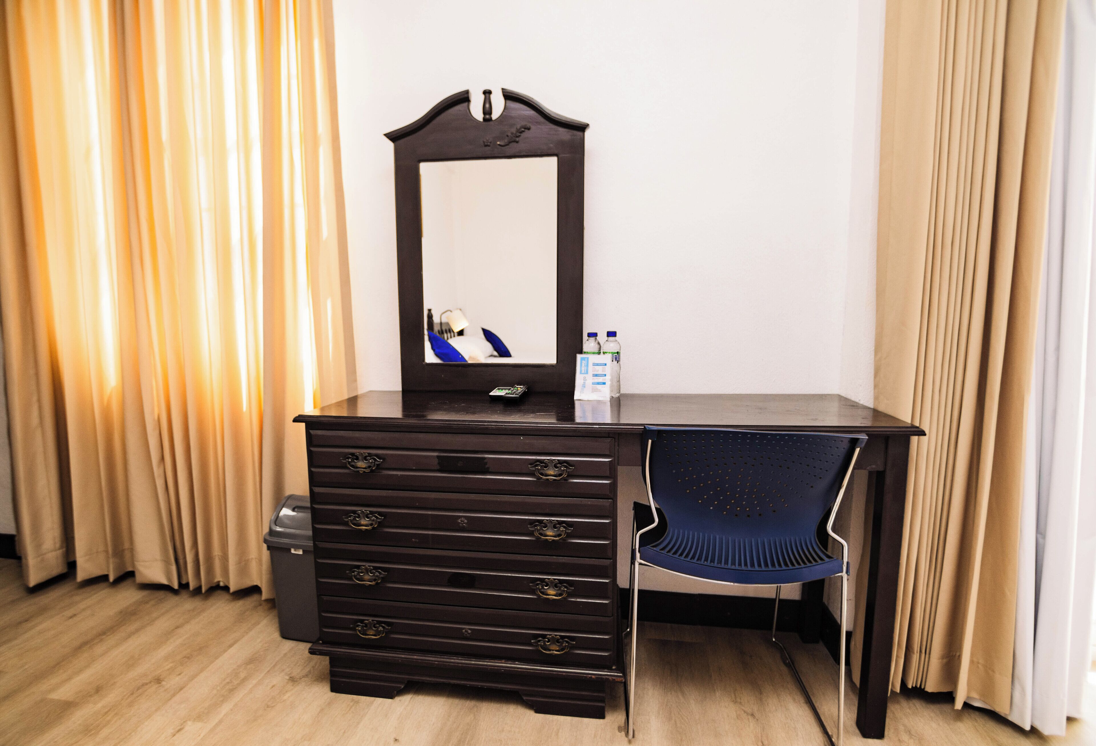 A room with a dark wooden desk, a chair, a dresser, and a mirror.