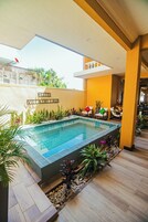 Una piscina con un borde de baldosas, rodeada de plantas y un pequeño rincón de estar con sillas.
