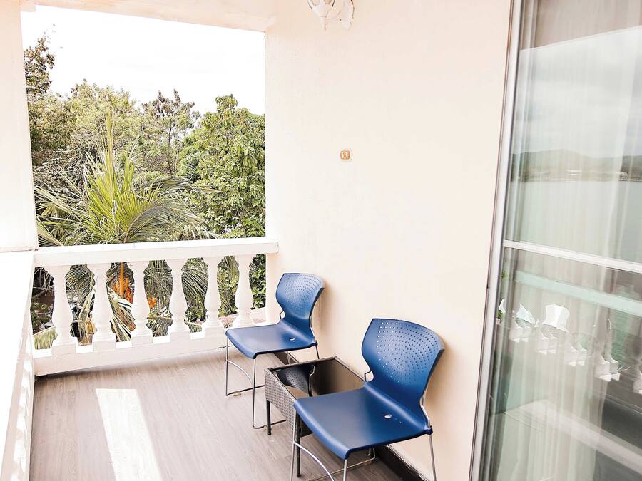 A balcony with two blue chairs, a white railing, and a view of greenery.