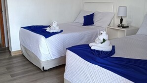 Two twin beds with white bedding and blue accents, a white nightstand with a lamp, and a framed picture on the wall. - Hotel Villa del Lago (Flores)