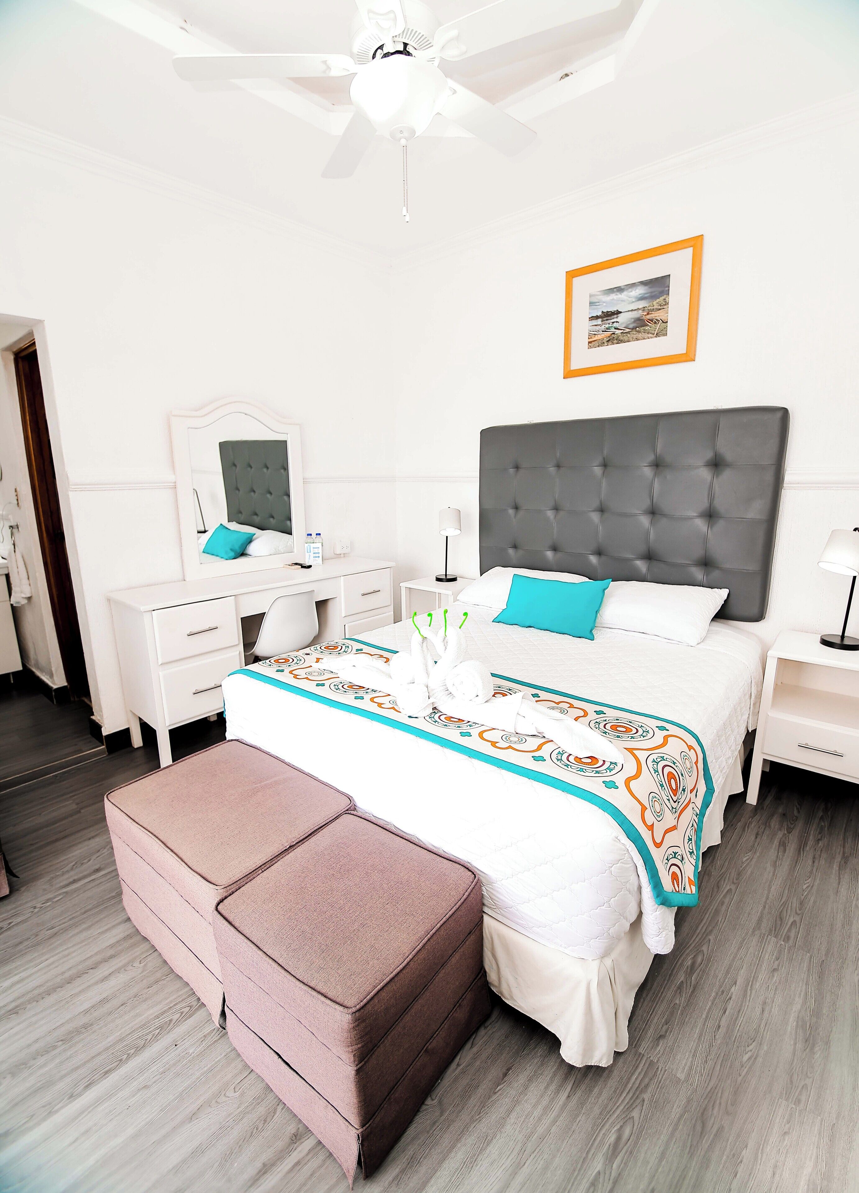 Quarto de hotel bem arrumado com cama, mesas de cabeceira, espelho e ventoinha no teto.