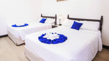 Habitación de hotel con dos camas, ropa de cama blanca, ventilador de techo y un cuadro en la pared.