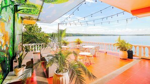 A terrace with outdoor seating, potted plants, and a view of the sea. - Hotel Villa del Lago (Flores)