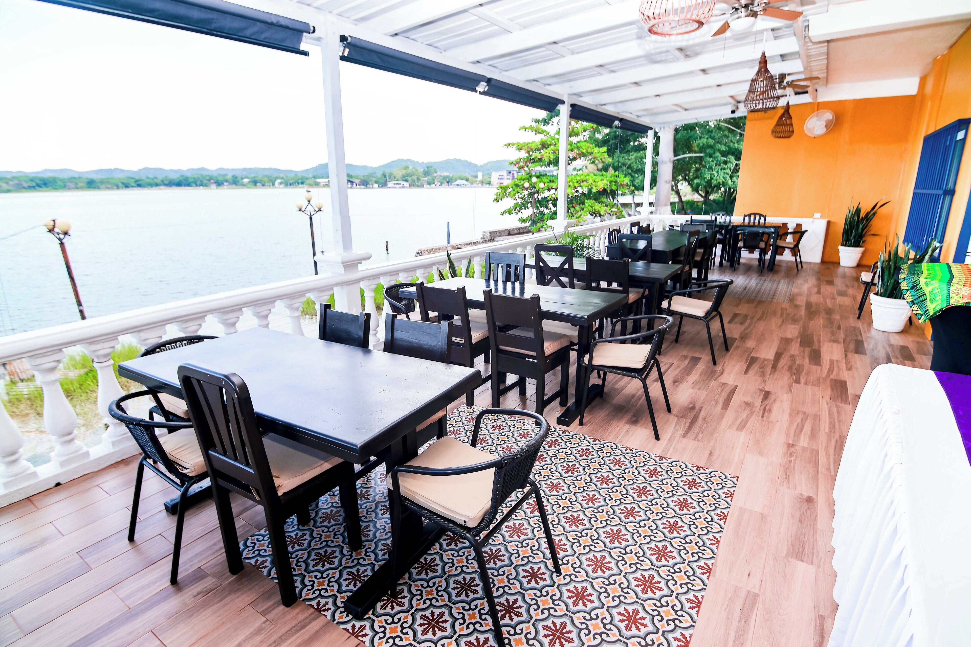 A covered outdoor dining area with tables and chairs, overlooking a body of water.
