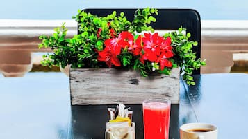 A table with breakfast items, a flower arrangement, and a view of a boat on water.