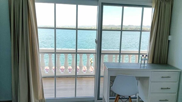 A room with a desk, chair, and a view of the sea through large windows. - Hotel Villa del Lago (Flores)