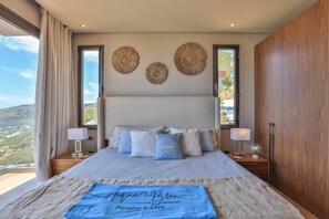 A bedroom with a large bed, two bedside tables, a wooden wardrobe, and a view of the outdoors.