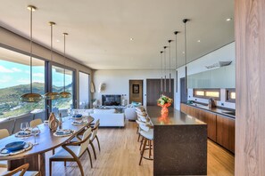 A modern kitchen with a large island, a dining area with a view, and a living room with a TV.