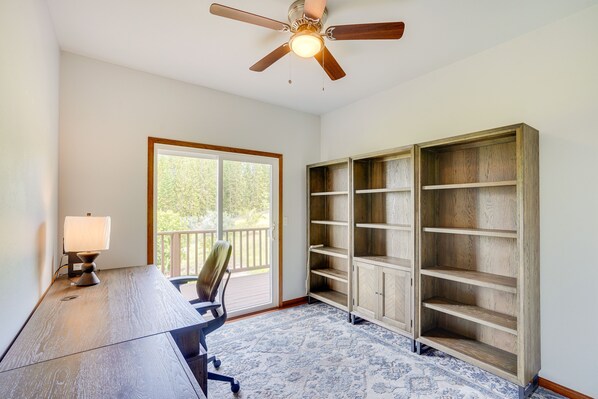 A room with a wooden desk, a chair, a ceiling fan, and built-in wooden shelves.