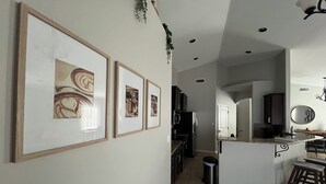 A kitchen with a central island, a refrigerator, and a microwave. There are framed pictures on the wall and a plant hanging above. - Spacious 4-bedroom house in charming Carlsbad with WiFi and AC (Carlsbad)