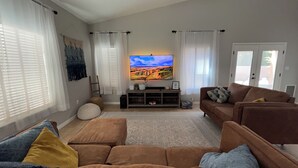 A living room with a large flat-screen TV, brown sofas, and a patterned rug. - Spacious 4-bedroom house in charming Carlsbad with WiFi and AC (Carlsbad)
