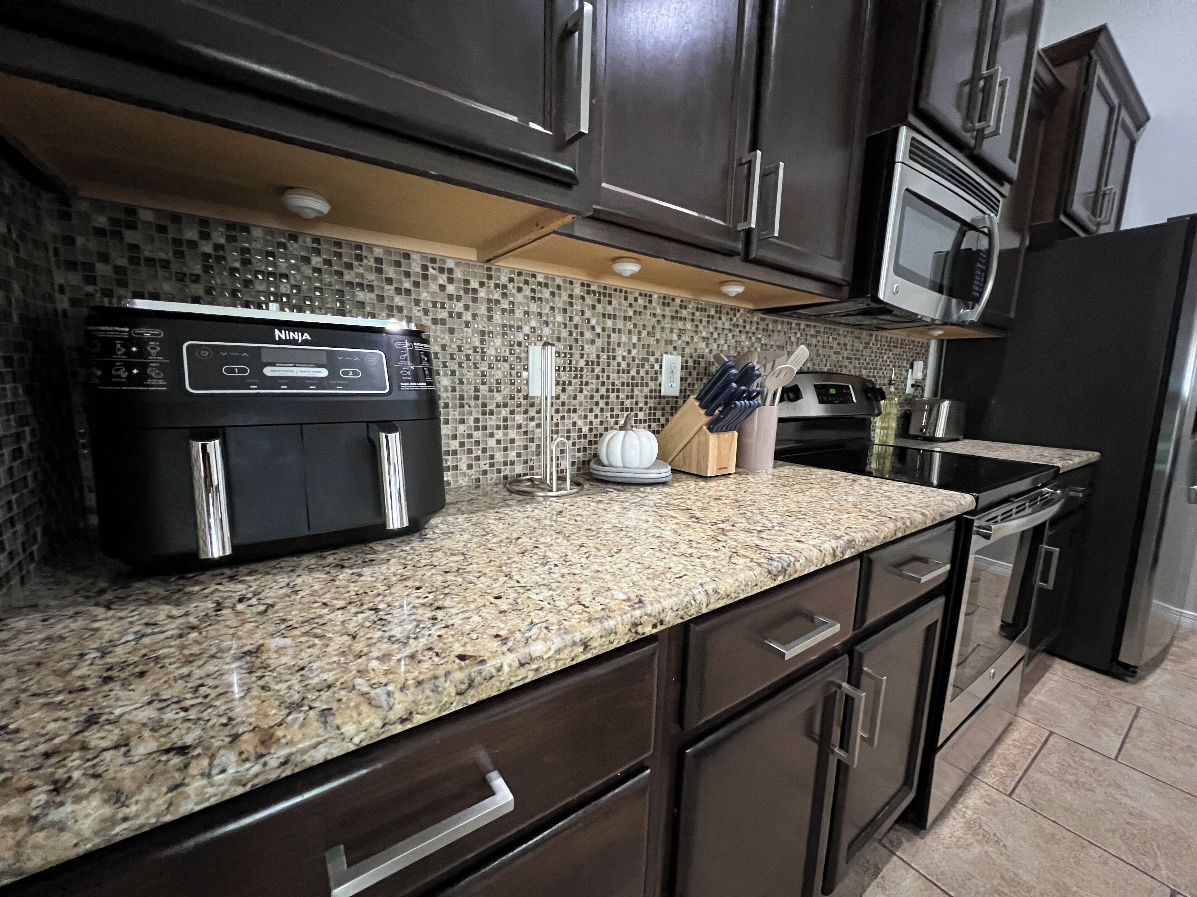 Una cocina con gabinetes de madera oscura, encimera de granito, microondas integrado y refrigerador de acero inoxidable.