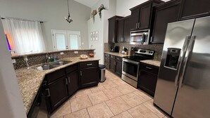 A modern kitchen with dark cabinetry, stainless steel appliances, and a granite countertop. - Spacious 4-bedroom house in charming Carlsbad with WiFi and AC (Carlsbad)
