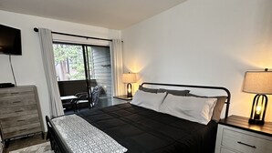 Un dormitorio con una cama grande, un escritorio, una silla, un televisor y una ventana con cortinas.