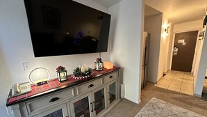 Una sala de estar con un televisor de pantalla plana montado en la pared, una chimenea con puertas de vidrio, un camino de mesa a cuadros rojo y negro, y una corona decorativa.