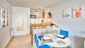 A modern kitchen with a central island, a dining area with blue chairs, and artwork on the walls. - Düne 1, Ferienwohnung 11 (Cuxhaven)