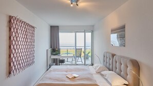 A modern bedroom with a large bed, a glass coffee table, and a view of the outdoors. - Düne 1, Ferienwohnung 11 (Cuxhaven)