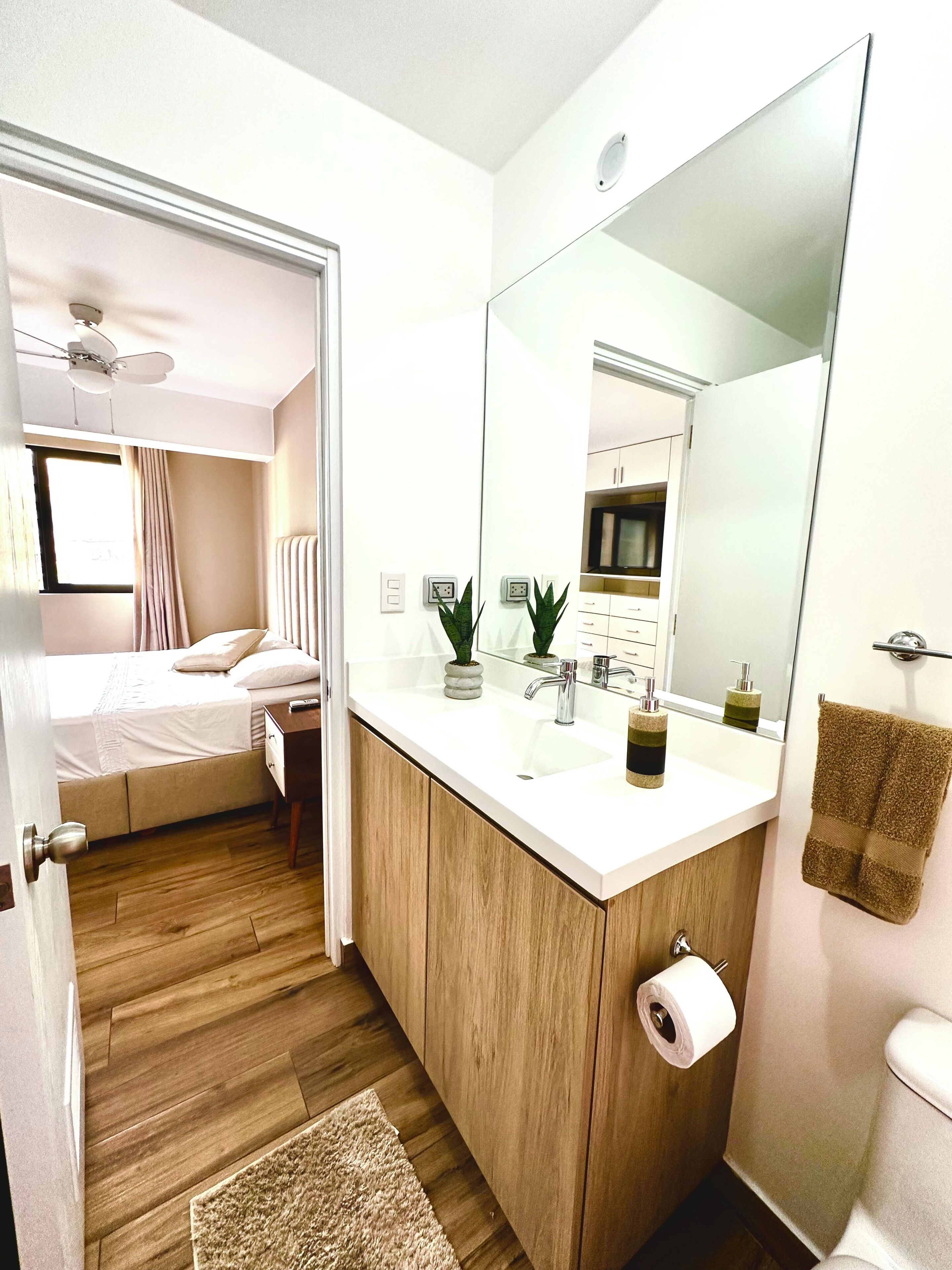 Un baño moderno con un espejo grande, armarios de madera, un lavabo blanco y un inodoro.