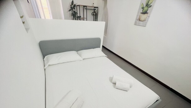 A neatly made bed with white linens and two rolled towels, a grey headboard, and a small potted plant on the wall. - Suite Menotti - Sanremo (Sanremo)
