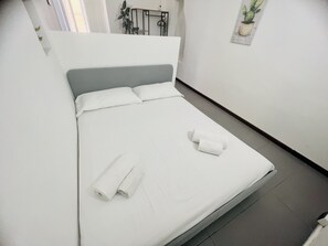 A neatly made bed with white linens and two rolled towels, a grey headboard, and a small potted plant on the wall. - Suite Menotti - Sanremo (Sanremo)