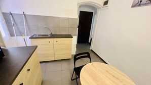 A compact kitchen with a sink, wooden cabinets, a black chair, and a small table. - Suite Menotti - Sanremo (Sanremo)