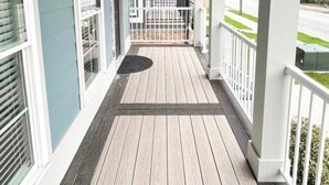 Eine Veranda mit Überdachung, Deckenventilator, Holzboden und weißen Geländern.