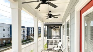 Une véranda couverte avec un ventilateur de plafond, une porte rouge et une vue sur la rue.