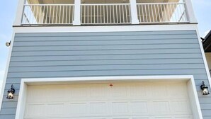Une maison à deux étages avec une porte de garage blanche, un balcon avec des balustrades blanches et deux appliques murales.
