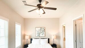Une chambre à coucher avec un lit, deux tables de chevet, un ventilateur de plafond et une fenêtre.