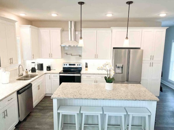 A modern kitchen with white cabinetry, a granite countertop, stainless steel appliances, and pendant lighting.