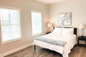 A bedroom with a bed, two bedside tables, a window, and a wall-mounted artwork.