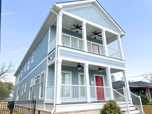 A two-story house with a red door, white railings, and two balconies with ceiling fans.