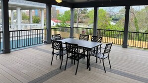 A covered outdoor patio with a table and chairs, ceiling fans, and a view of a pool and buildings.