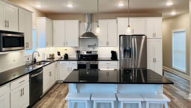Una cocina moderna con armarios blancos, electrodomésticos de acero inoxidable y una isla con encimera negra.