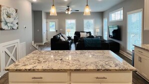 A spacious kitchen with a marble countertop, pendant lighting, and a ceiling fan.