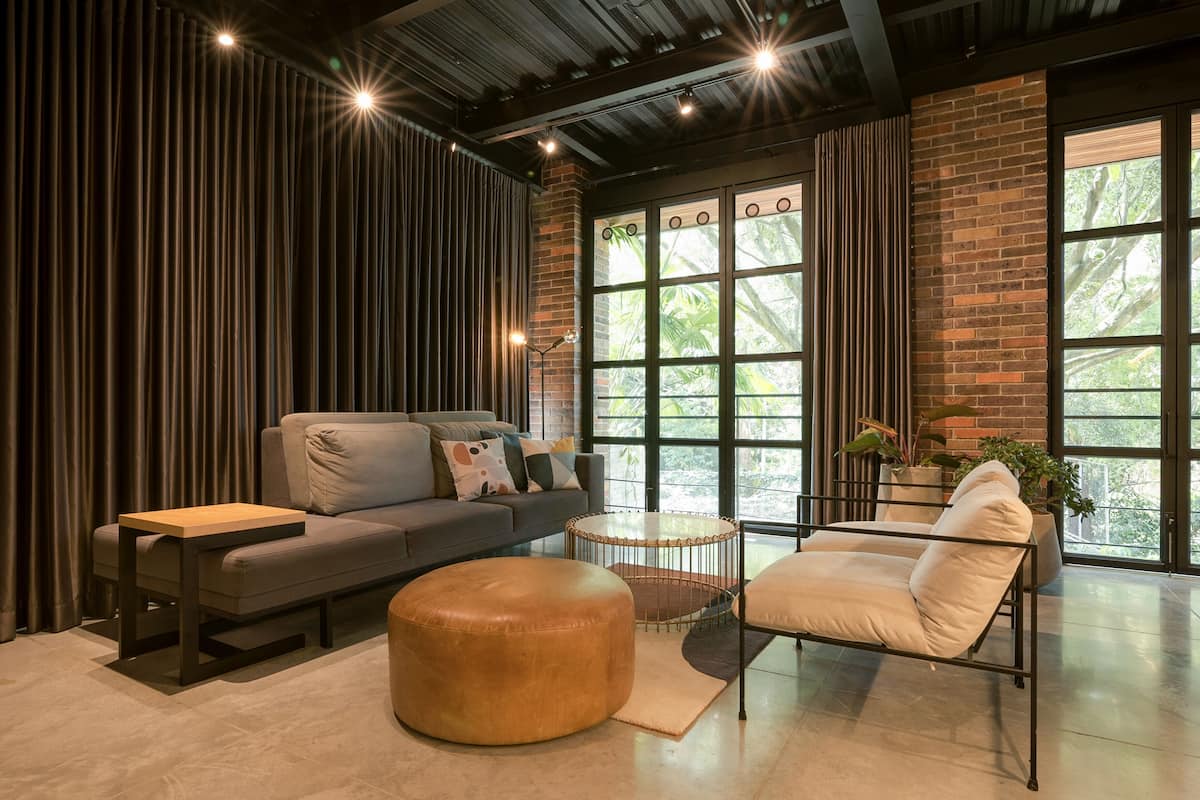 A modern living room with a sofa, ottoman, and chair, a small round table, and large windows with a view of greenery.